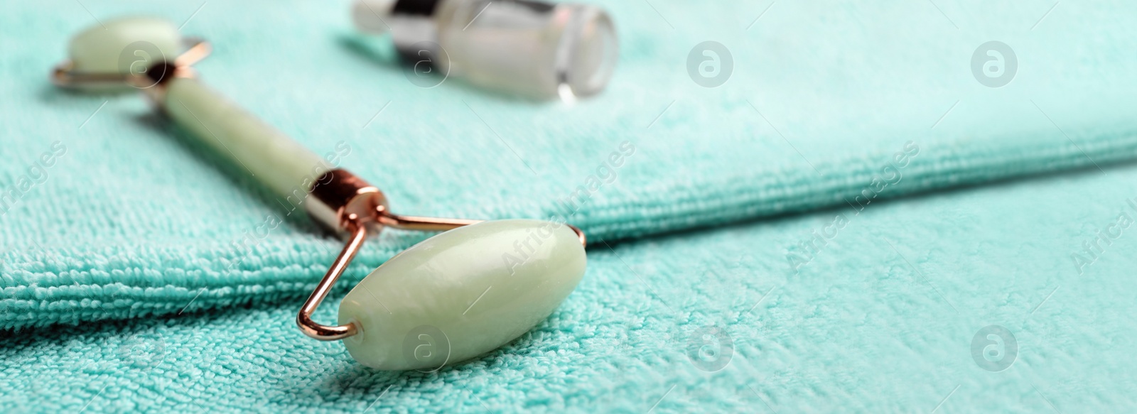 Image of Natural jade face roller on towel, closeup view. Banner design