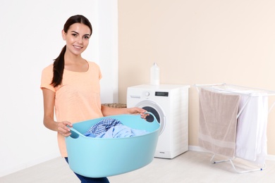 Photo of Young woman with laundry basket near washing machine at home. Space for text