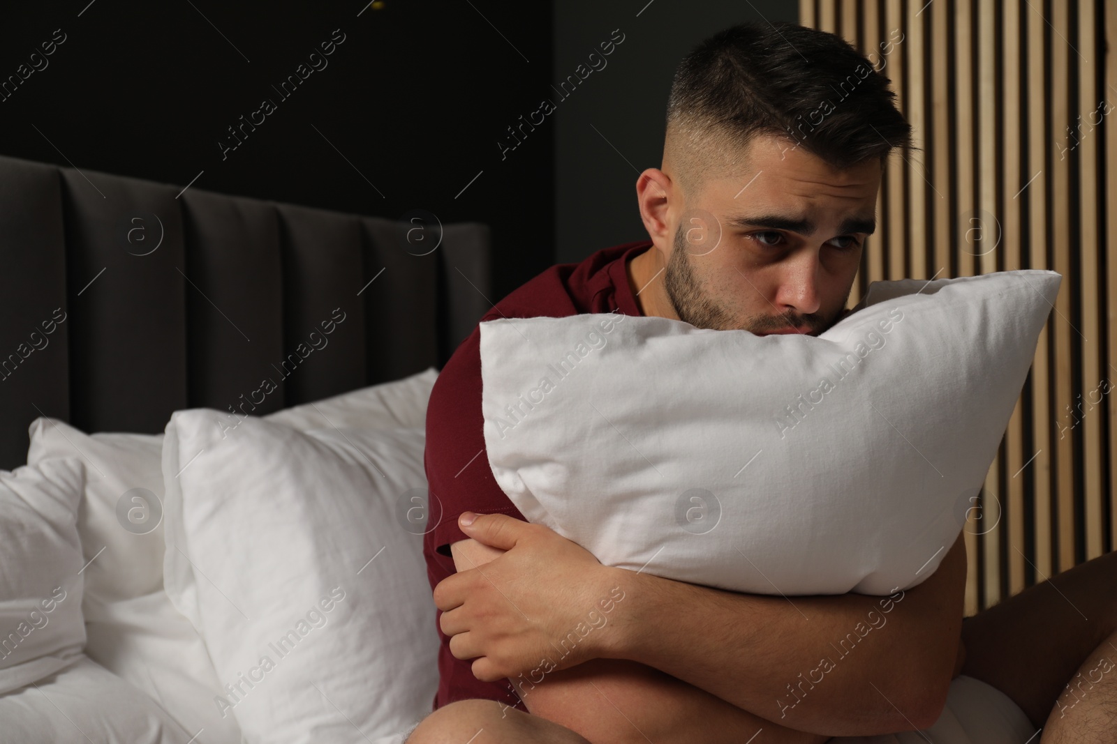 Photo of Sad man hugging pillow on bed at home. Space for text