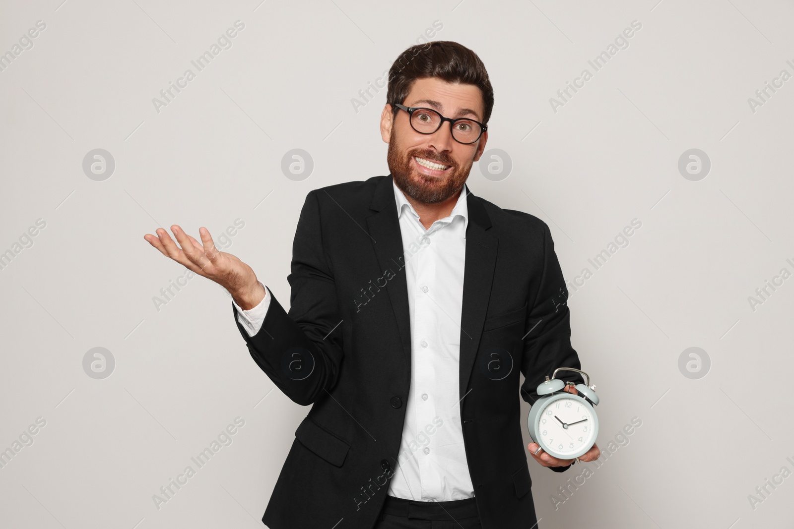 Photo of Emotional bearded man with alarm clock on light grey background. Being late concept