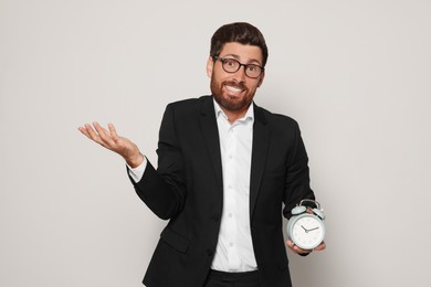 Emotional bearded man with alarm clock on light grey background. Being late concept