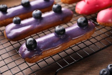 Cooling rack with different tasty glazed eclairs on wooden table, closeup