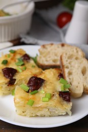 Photo of Tasty sausage casserole with green onion and bread on table, closeup