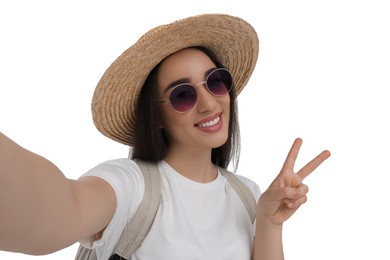 Photo of Smiling young woman in sunglasses and straw hat taking selfie and showing peace sign on white background
