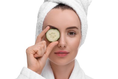 Beautiful woman in bathrobe covering eye with piece of cucumber on white background