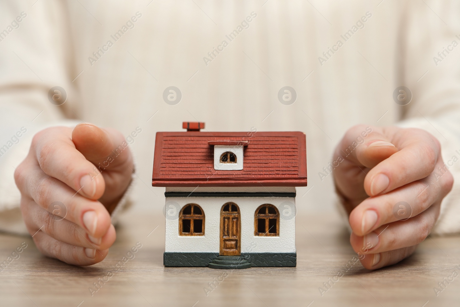 Photo of Home security concept. Woman with house model at wooden table, closeup