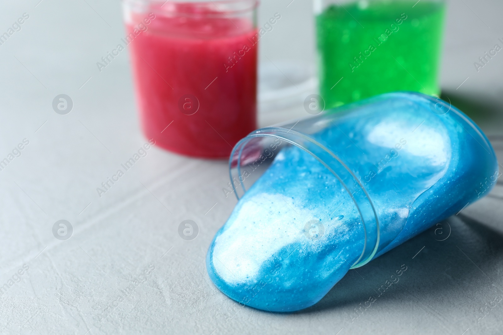 Photo of Overturned plastic container with light blue slime on grey background. Space for text