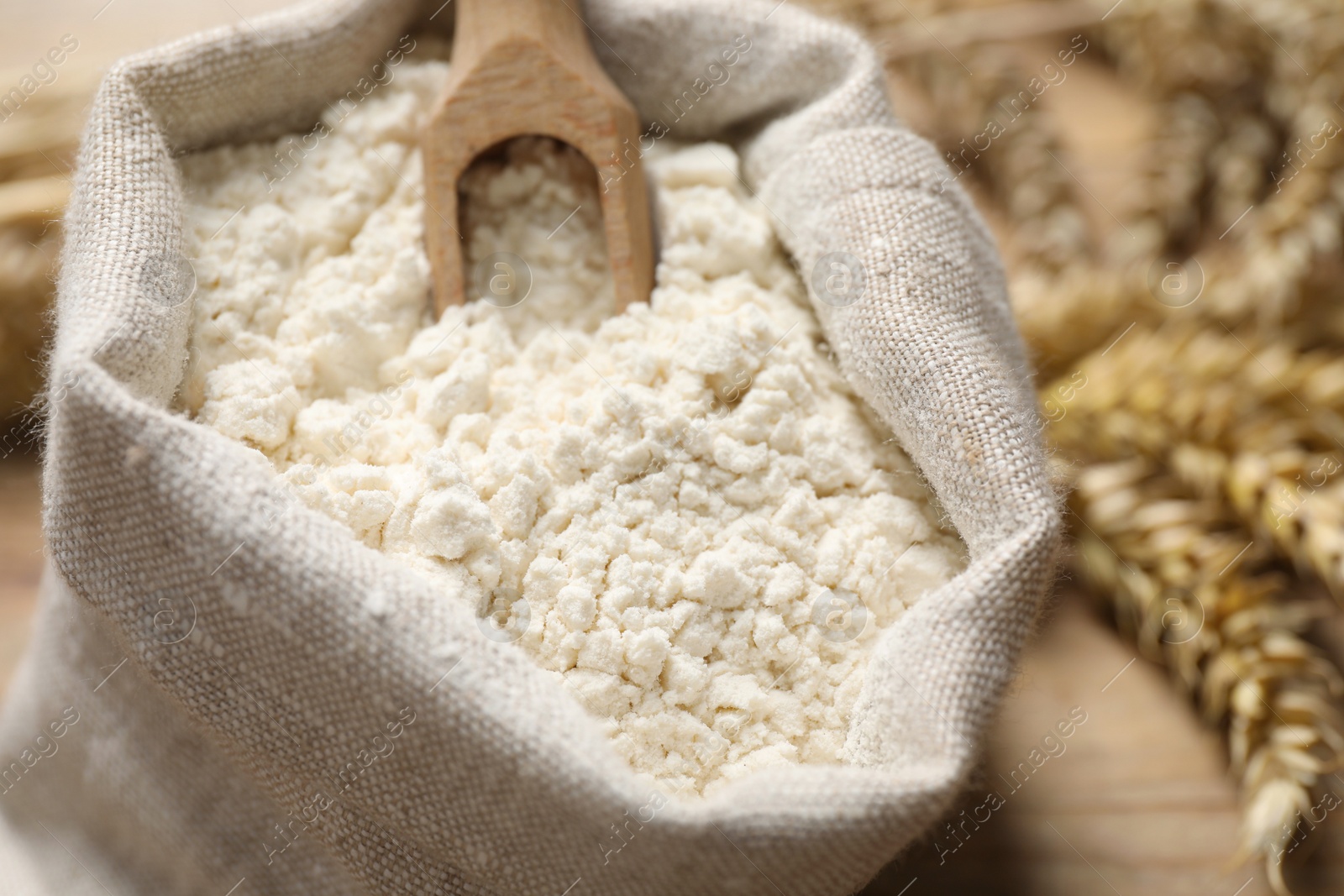 Photo of Wheat flour and wooden scoop in sack bag on table, closeup