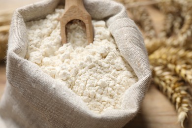 Wheat flour and wooden scoop in sack bag on table, closeup