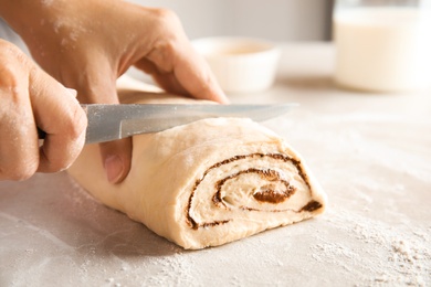 Photo of Woman cutting dough for cinnamon rolls at table, closeup