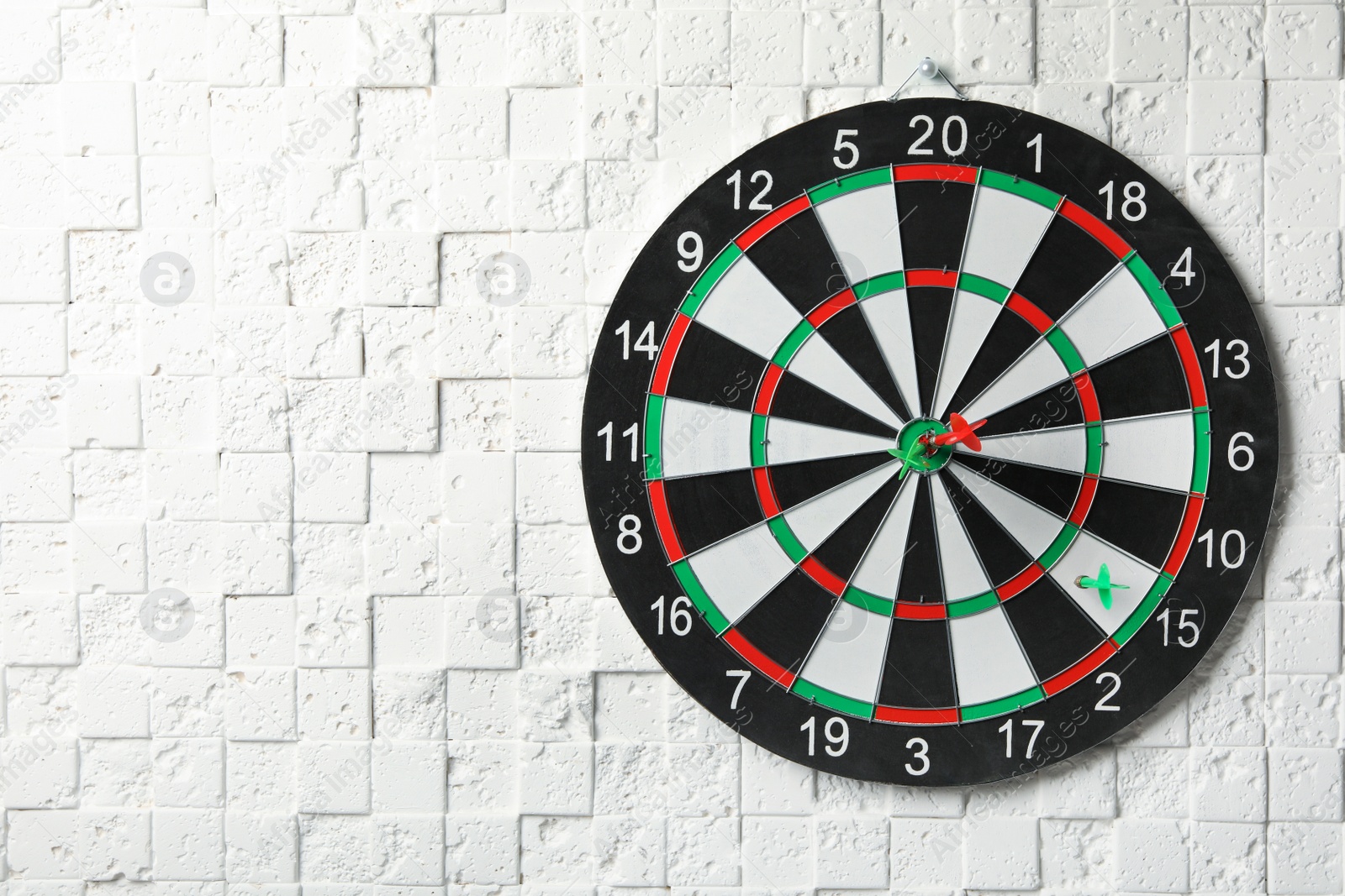 Photo of Arrows hitting dart board on white textured wall. Space for text