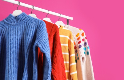 Collection of warm sweaters hanging on rack against color background