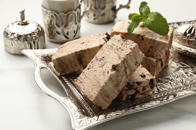 Photo of Tasty chocolate halva and mint on white marble table, closeup