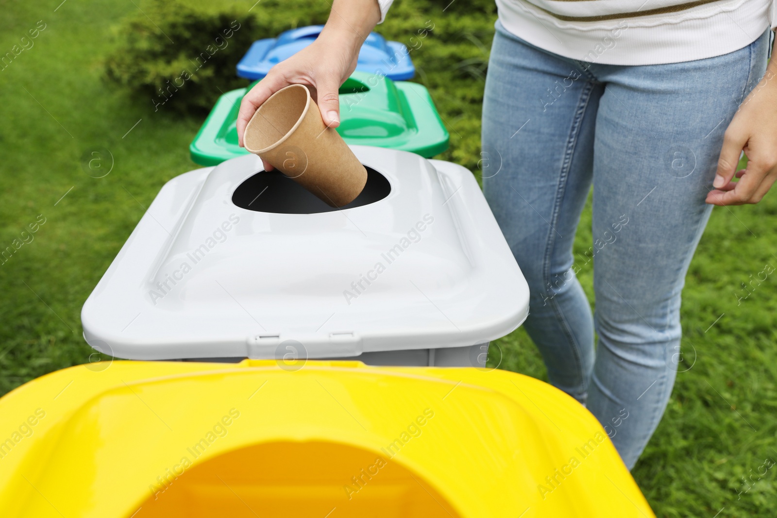 Photo of Woman throwing coffee cup into recycling bin outdoors, closeup