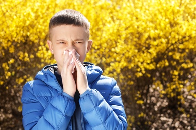 Photo of Little boy suffering from seasonal allergy outdoors, space for text