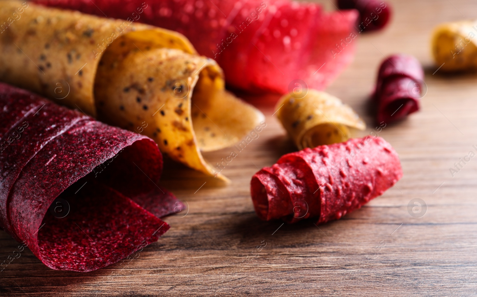 Photo of Delicious fruit leather rolls on wooden table, closeup