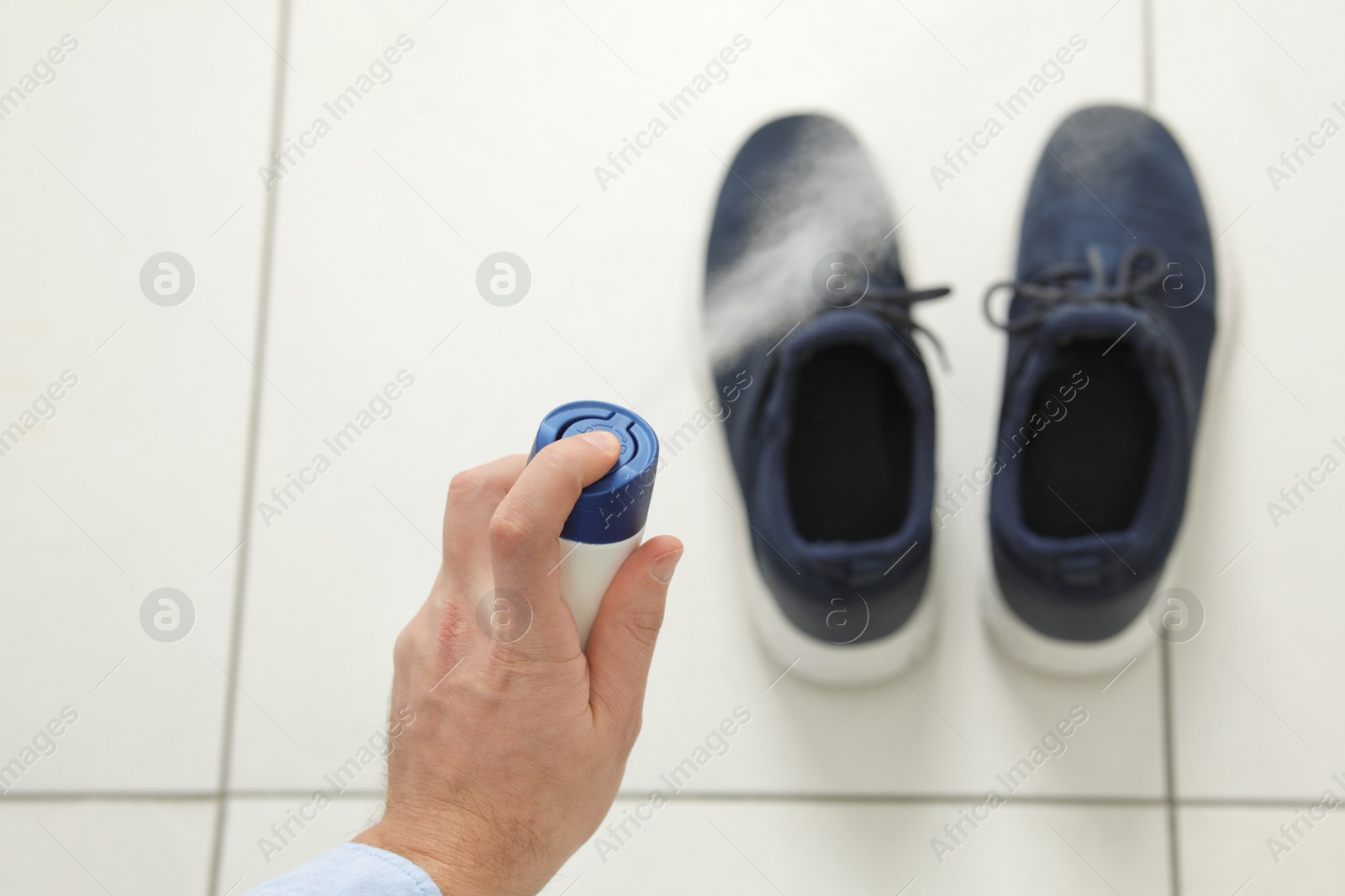 Photo of Man spraying deodorant over pair of shoes at home, closeup