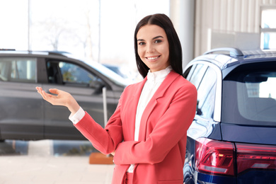 Happy young saleswoman in modern car salon