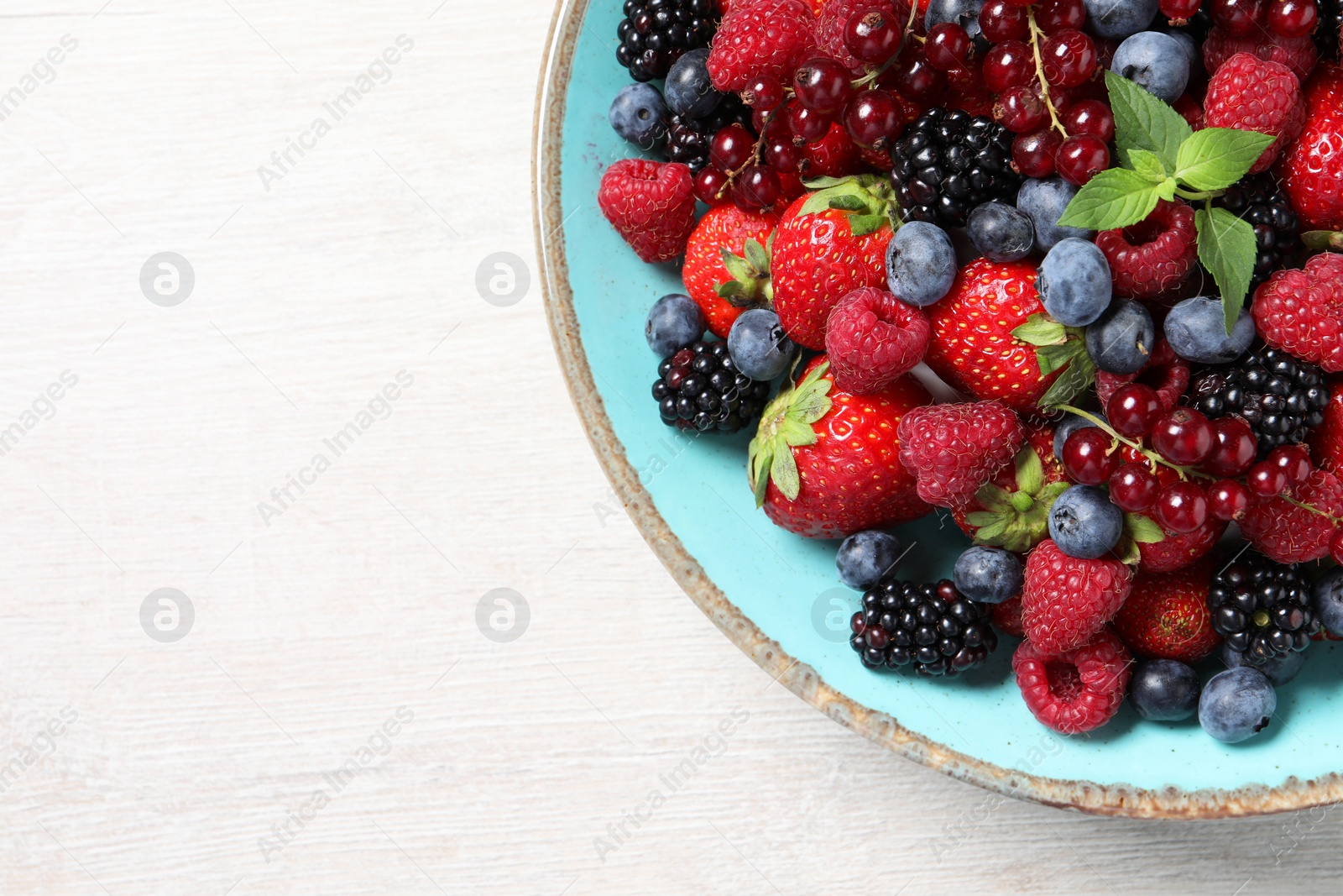 Photo of Many different fresh ripe berries in bowl on white wooden table, top view. Space for text