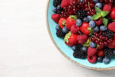 Many different fresh ripe berries in bowl on white wooden table, top view. Space for text