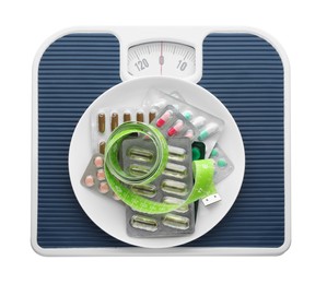 Scales with plate of pills and measuring tape on white background, top view