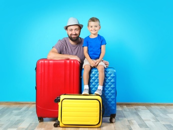Photo of Man and his son with suitcases near color wall. Vacation travel