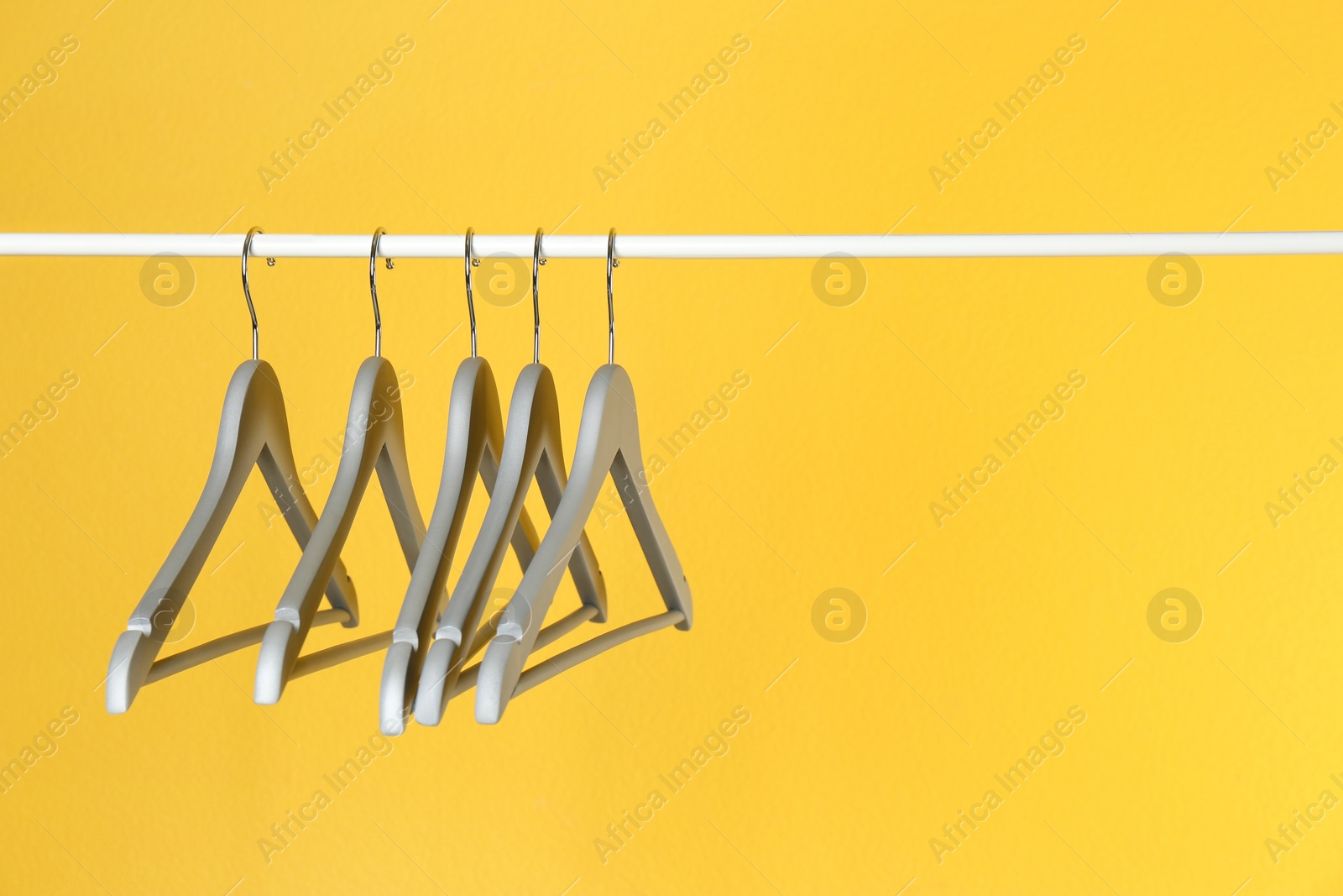 Photo of Metal rack with clothes hangers on color background, space for text