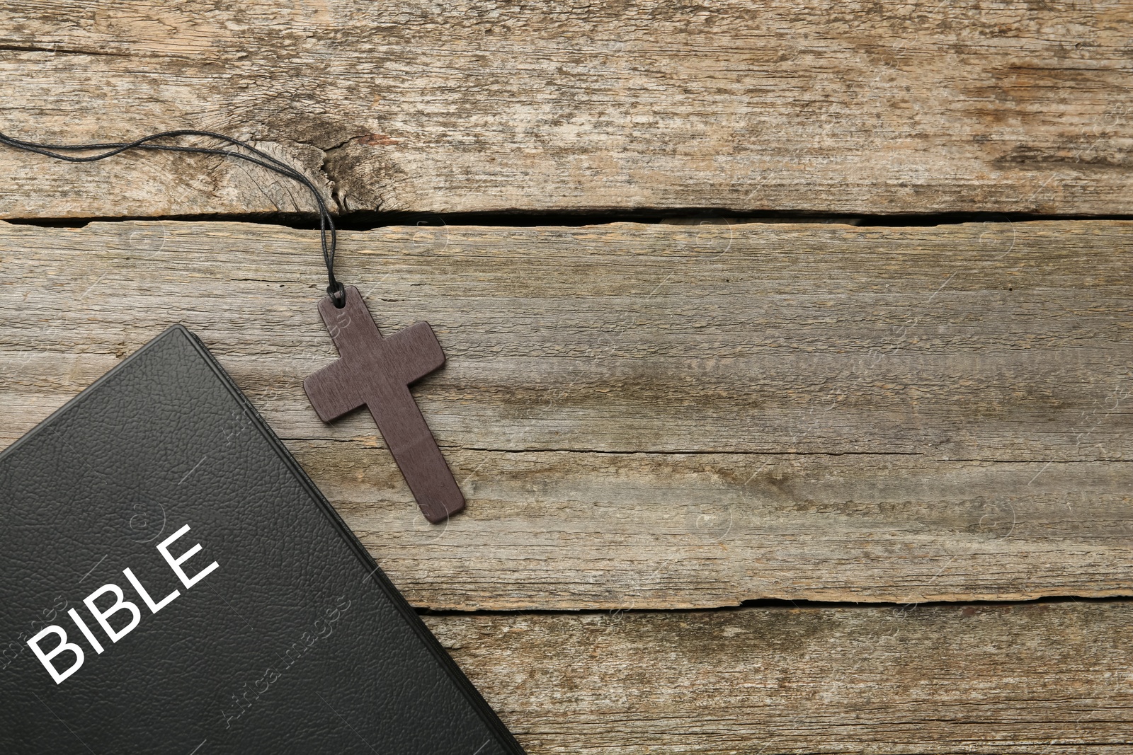 Photo of Christian cross and Bible on wooden table, flat lay. Space for text