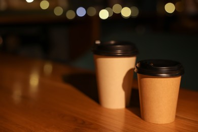 Photo of Paper coffee cups on wooden table in cafe. Space for text