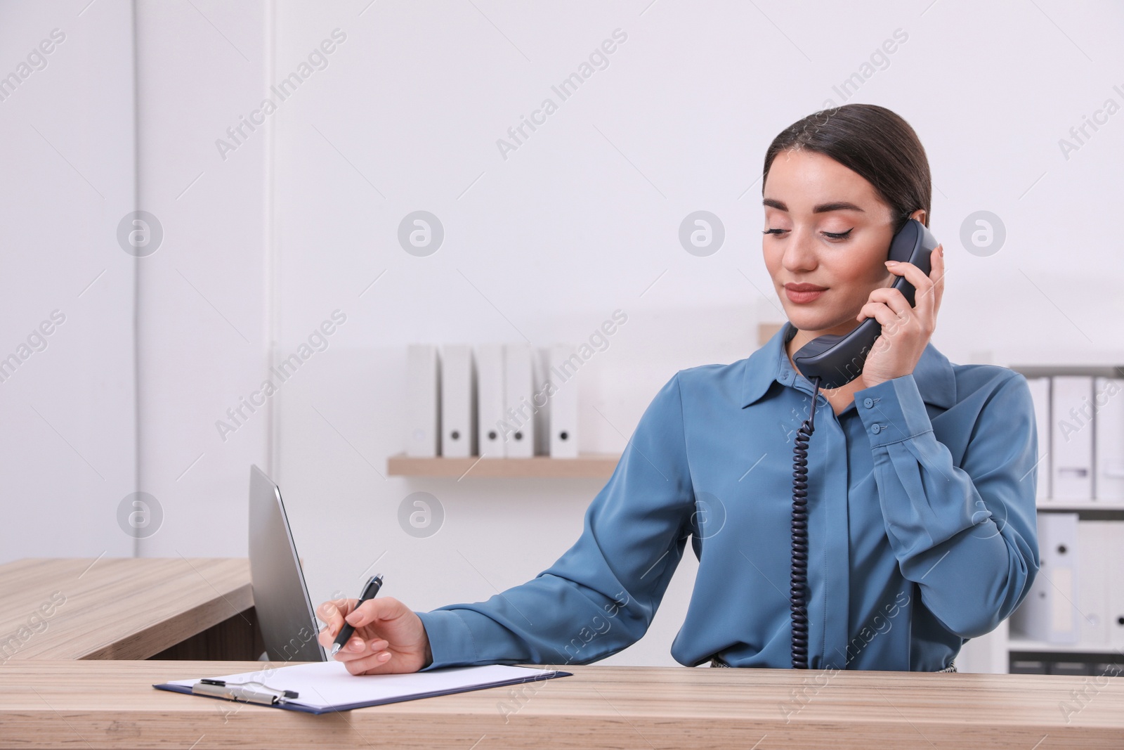 Photo of Female receptionist with clipboard talking on phone at workplace