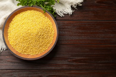 Photo of Millet groats in bowl and parsley on wooden table, top view. Space for text