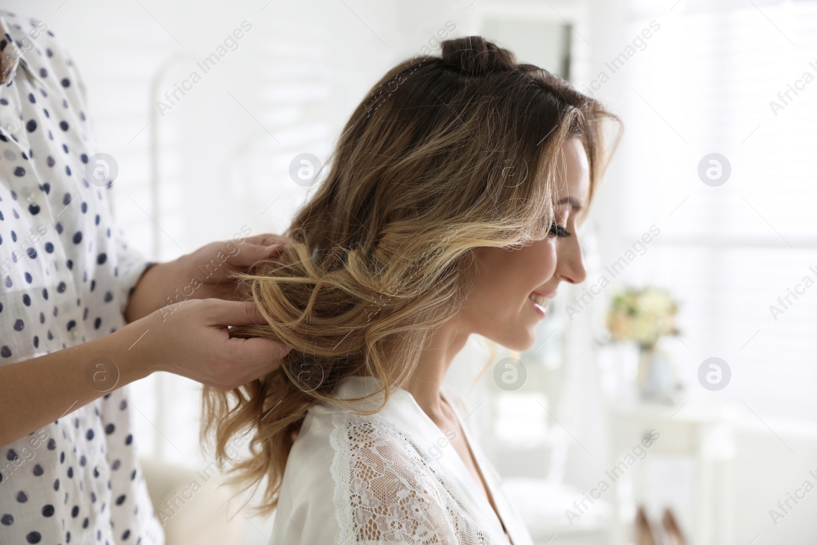 Photo of Professional stylist making wedding hairstyle for bride in salon