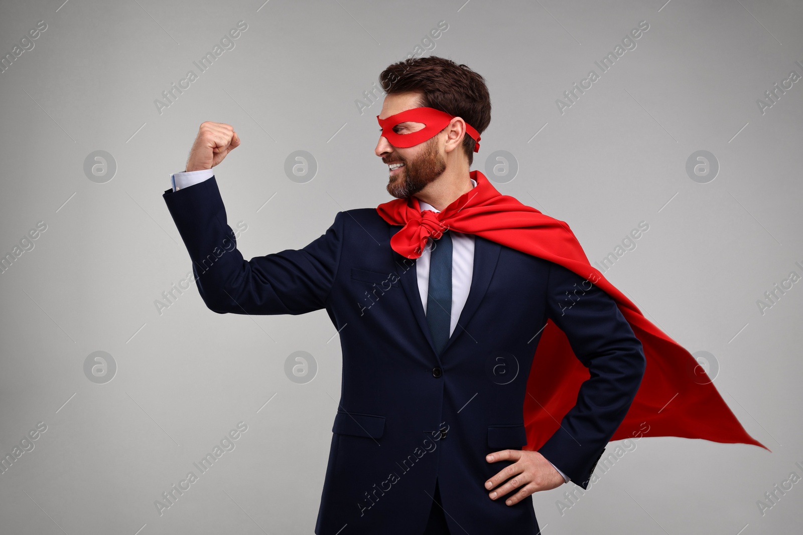 Photo of Happy businessman wearing red superhero cape and mask on beige background