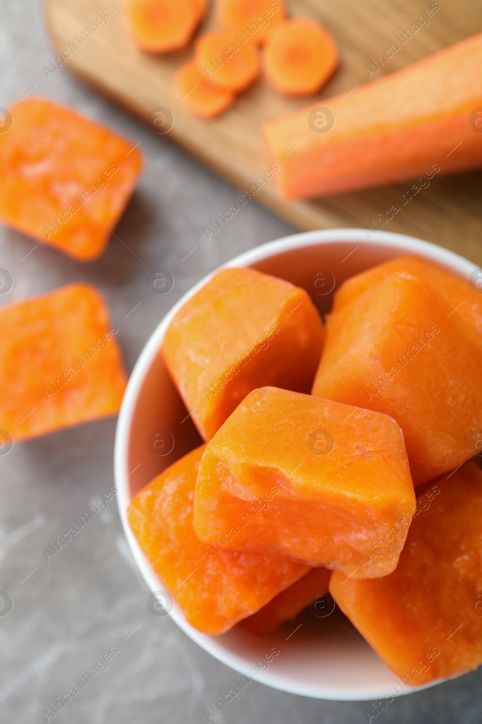 Photo of Bowl of frozen carrot puree cubes and ingredient on marble table, flat lay