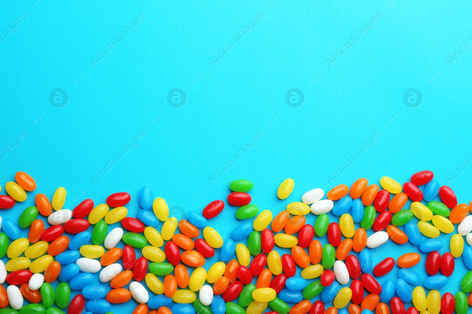 Photo of Colorful jelly beans on turquoise  background, flat lay. Space for text