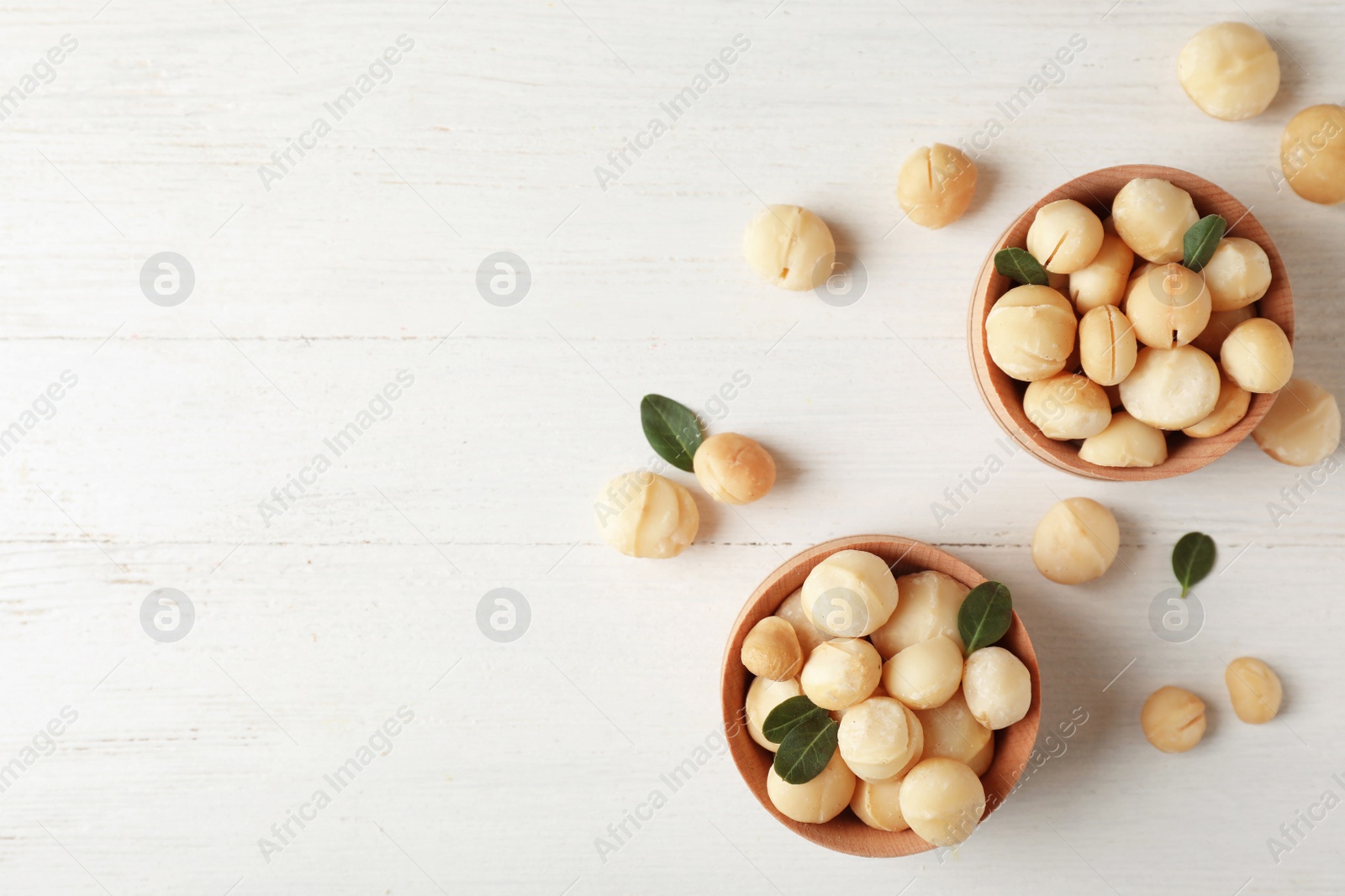 Photo of Bowls with shelled organic Macadamia nuts and space for text on white table, top view