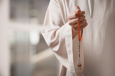 Muslim man with misbaha praying on blurred background, closeup. Space for text