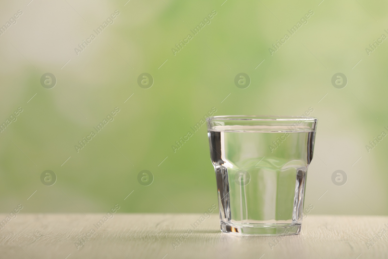 Photo of Glass of pure water on white wooden table against blurred background, space for text