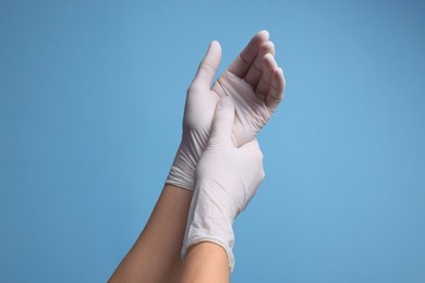 Photo of Doctor wearing white medical gloves on light blue background, closeup