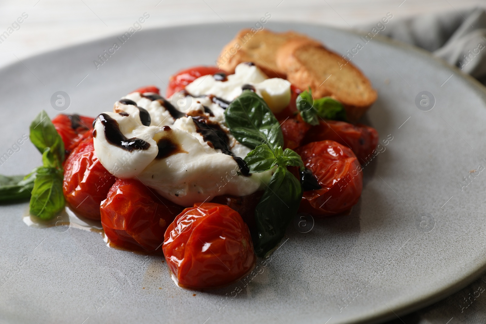 Photo of Delicious burrata cheese served with tomatoes, croutons and basil sauce on plate, closeup
