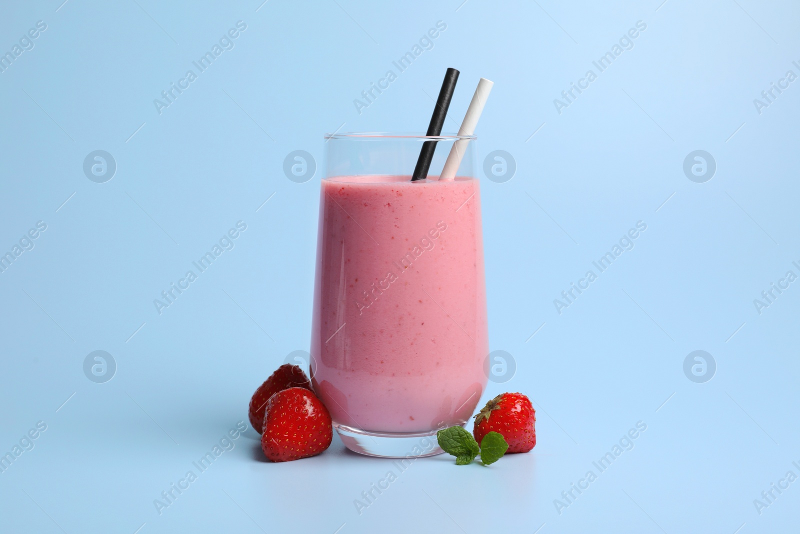 Photo of Glass with delicious berry smoothie and fresh strawberries on light blue background