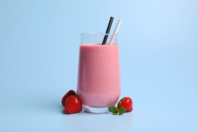 Glass with delicious berry smoothie and fresh strawberries on light blue background