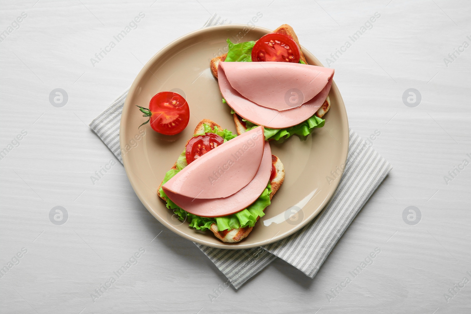 Photo of Plate of tasty sandwiches with boiled sausage, tomato and lettuce on white wooden table, top view