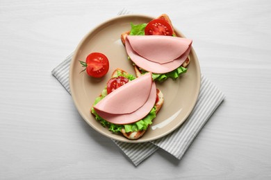 Plate of tasty sandwiches with boiled sausage, tomato and lettuce on white wooden table, top view