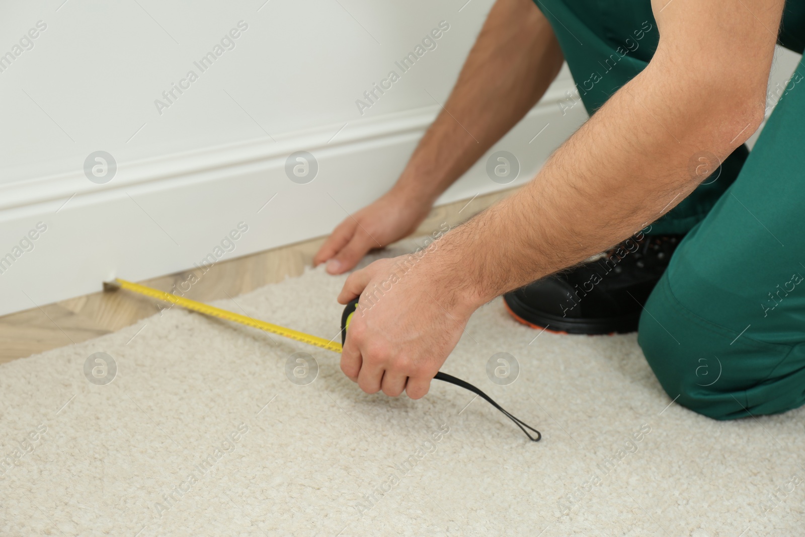 Photo of Worker with measuring tape installing new carpet indoors, closeup