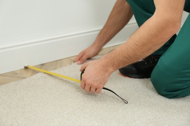 Photo of Worker with measuring tape installing new carpet indoors, closeup