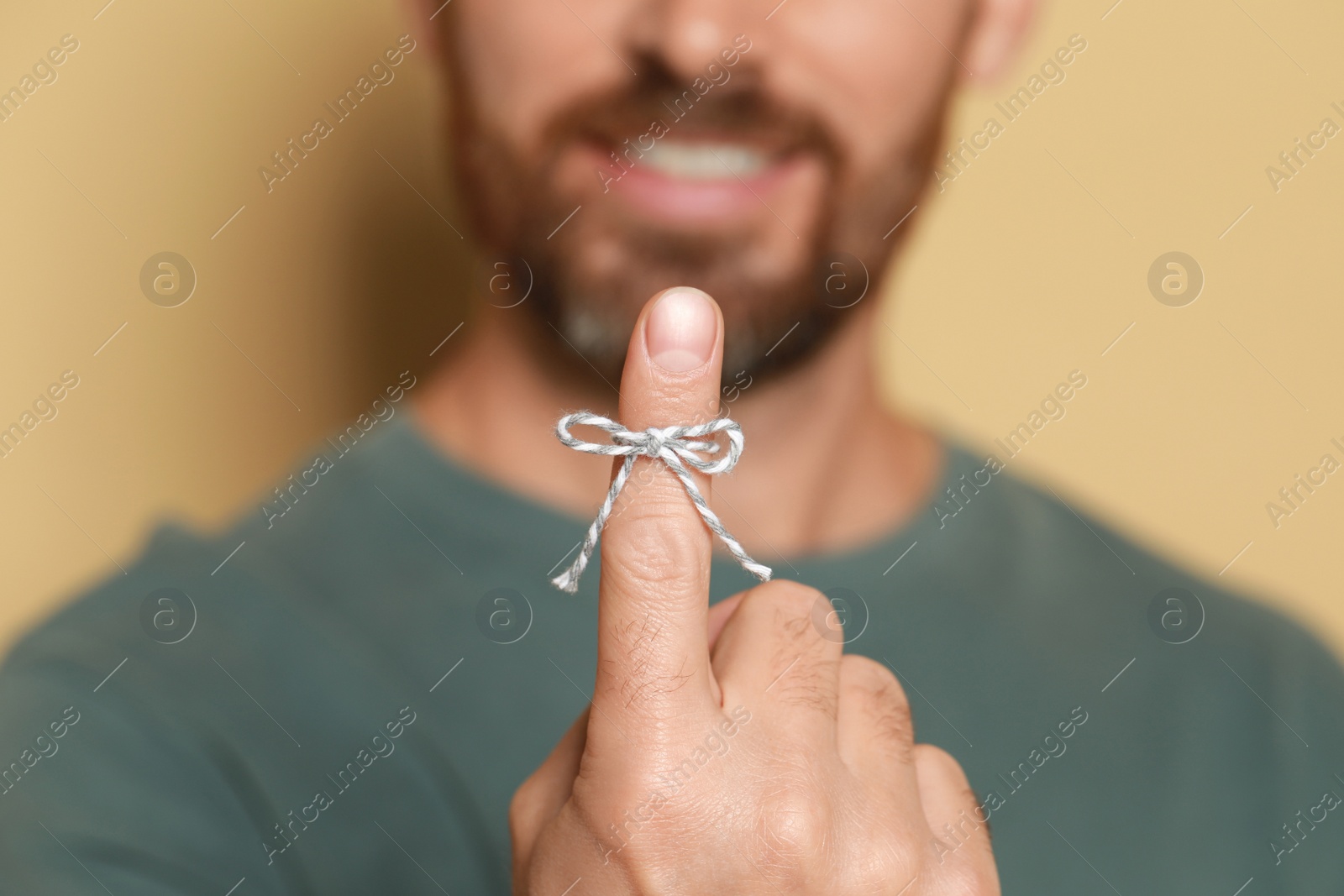 Photo of Man showing index finger with tied bow as reminder against beige background, focus on hand