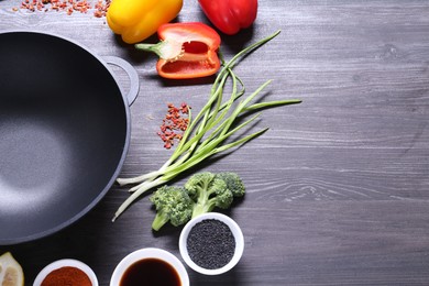 Photo of Empty iron wok and ingredients on dark grey wooden table. Space for text