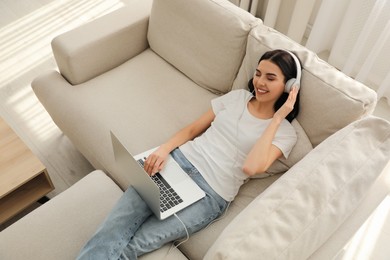 Woman with laptop and headphones lying on sofa at home