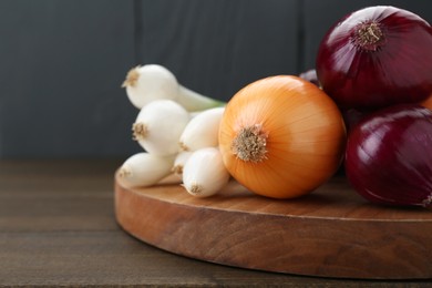 Board with different kinds of onions on wooden table, closeup. Space for text